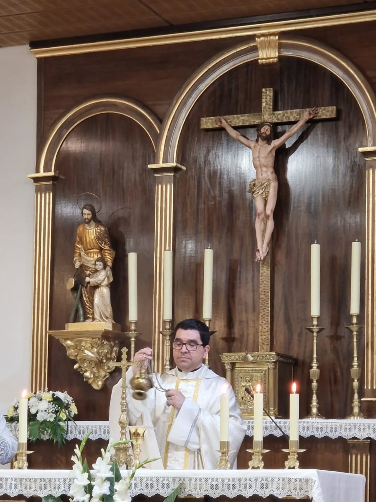 Celebrante con vestiduras blancas sostiene un incensario ante el altar y el crucifijo de San Bernardo